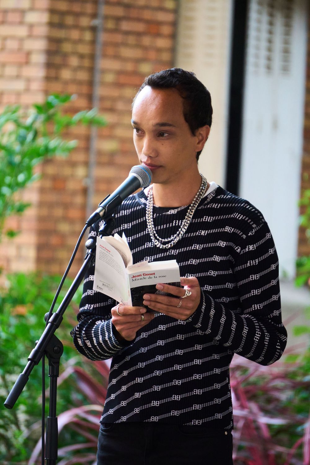 A person reading from a book at a microphone stand during an outdoor performance.