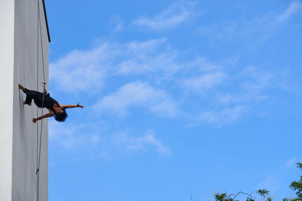 Silhouette of person performing aerial acrobatics against blue sky.