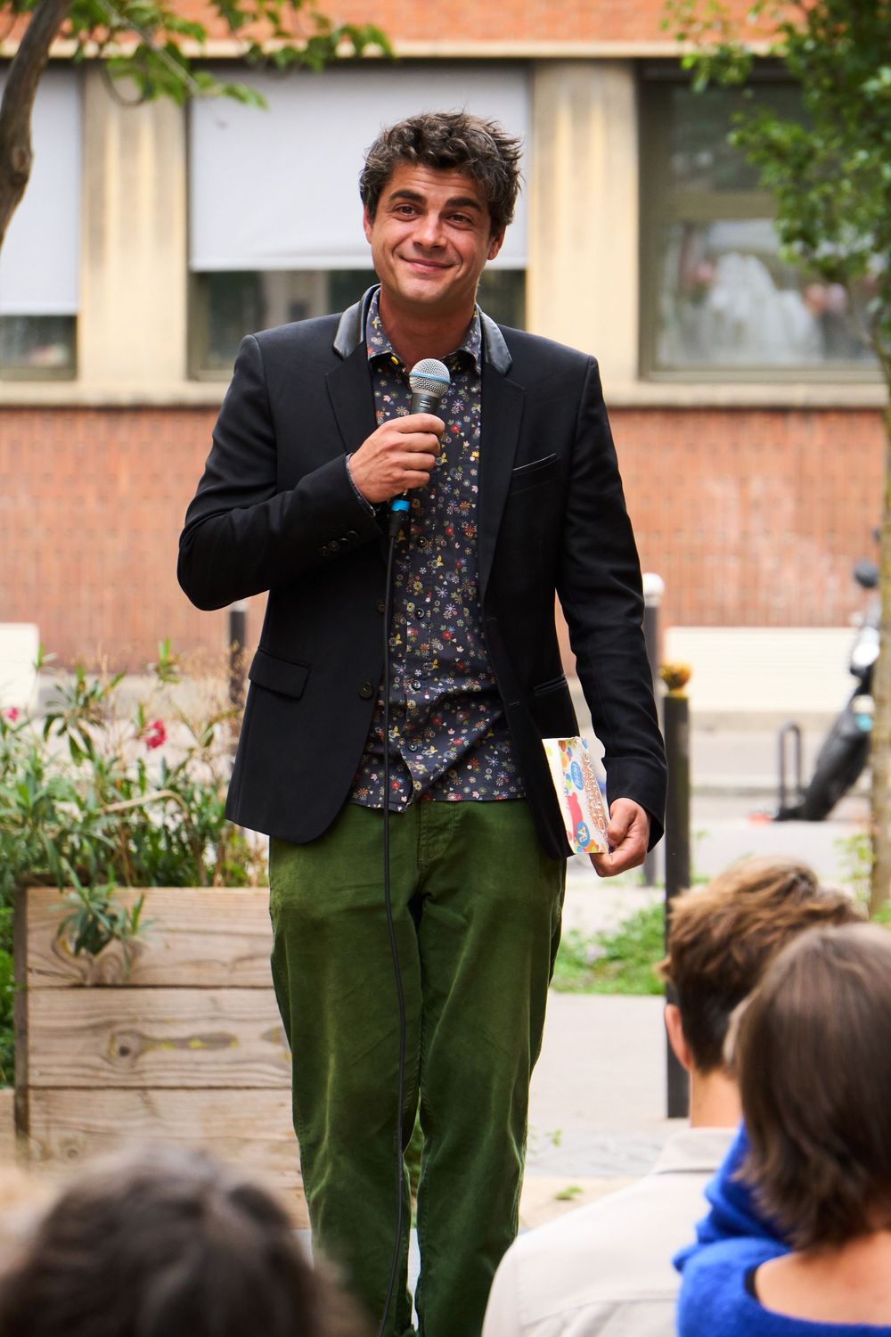 Person speaking into microphone while holding drink outdoors.