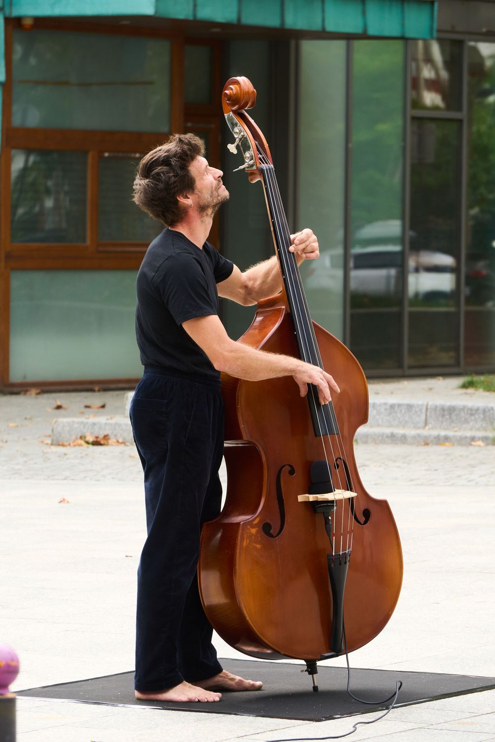 Musician playing upright bass outdoors in casual attire.