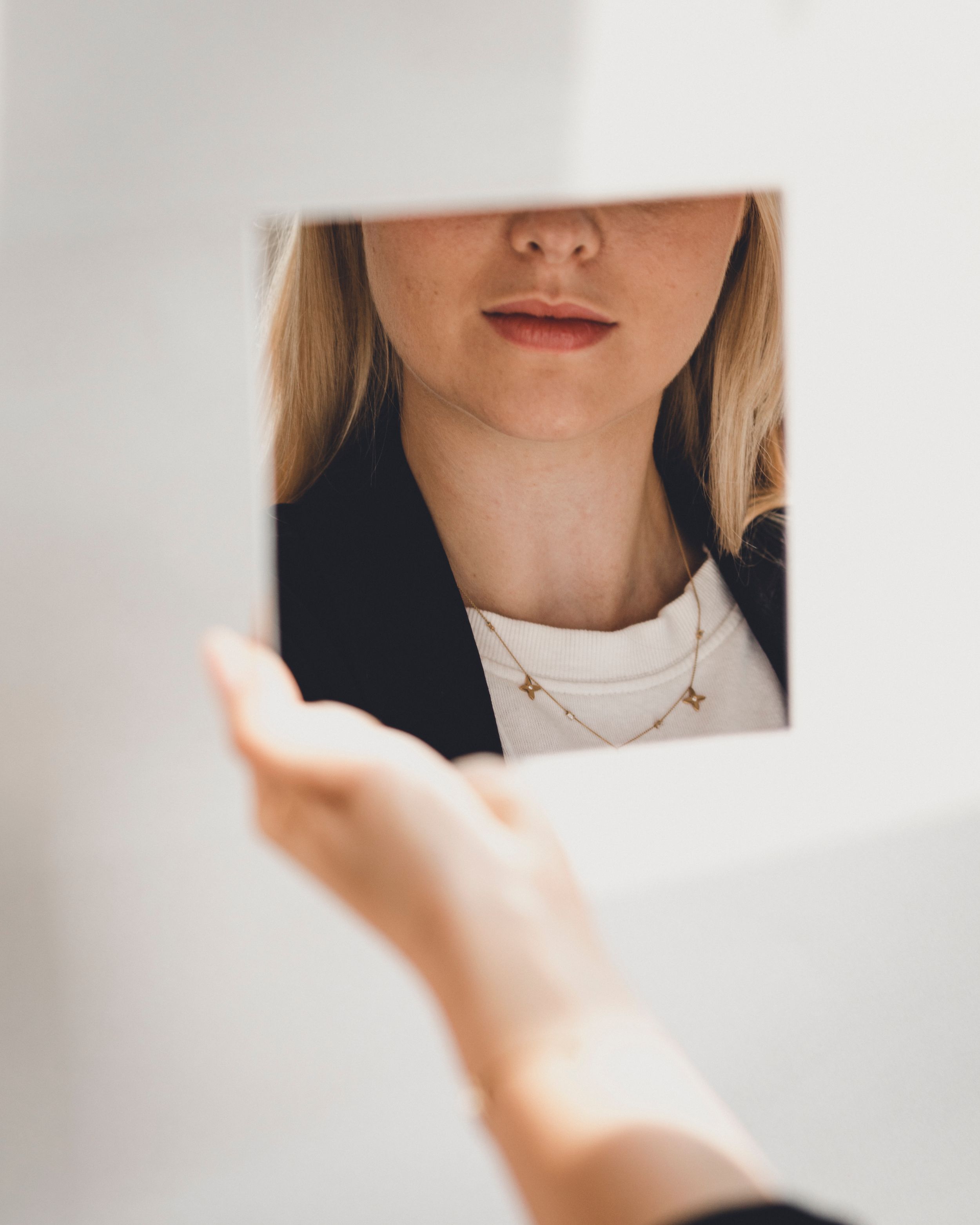 Close-up of delicate layered necklaces worn with white top and black blazer reflected in mirror.