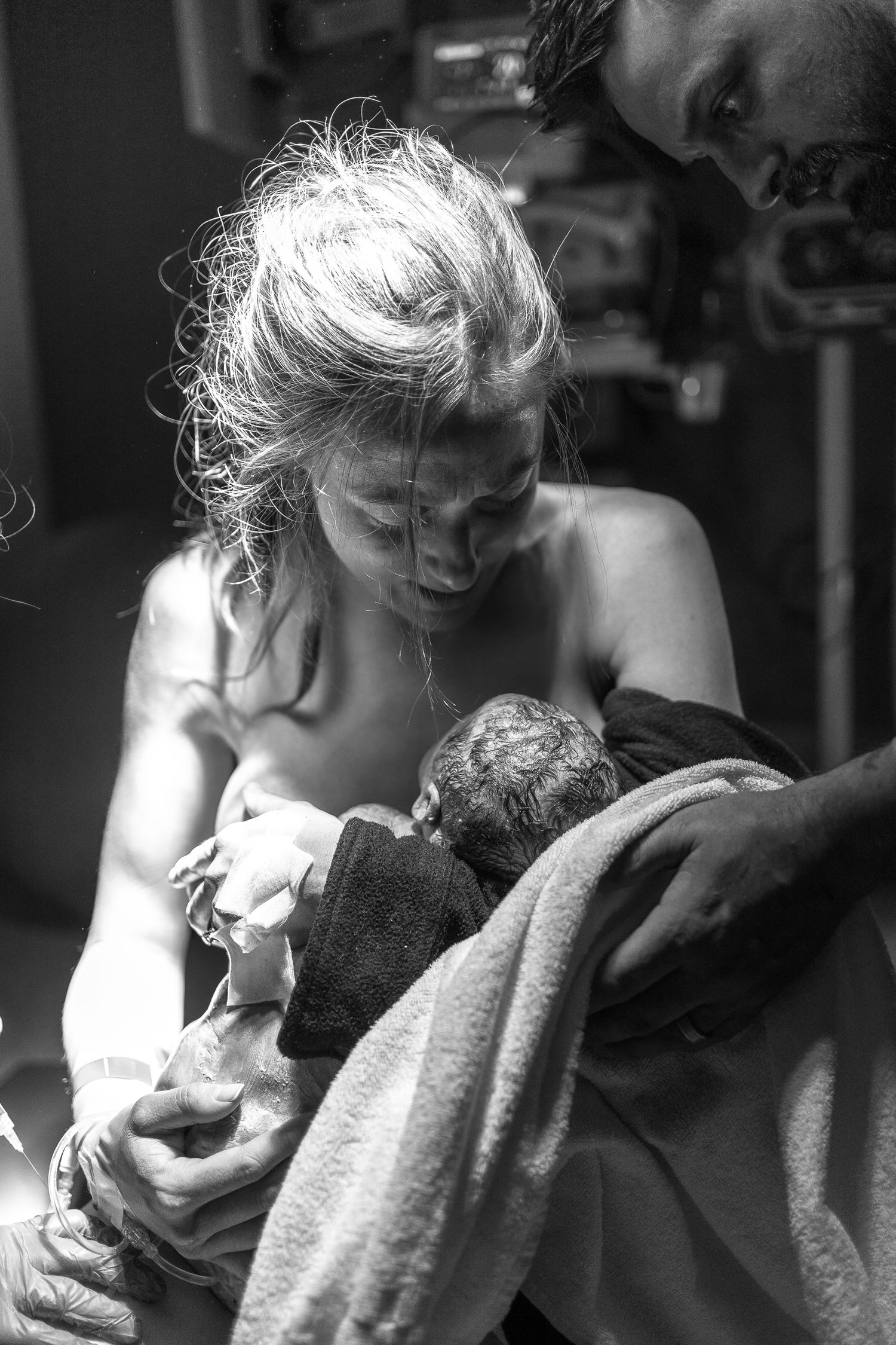 A tender black and white moment of a mother cradling a newborn wrapped in blankets.
