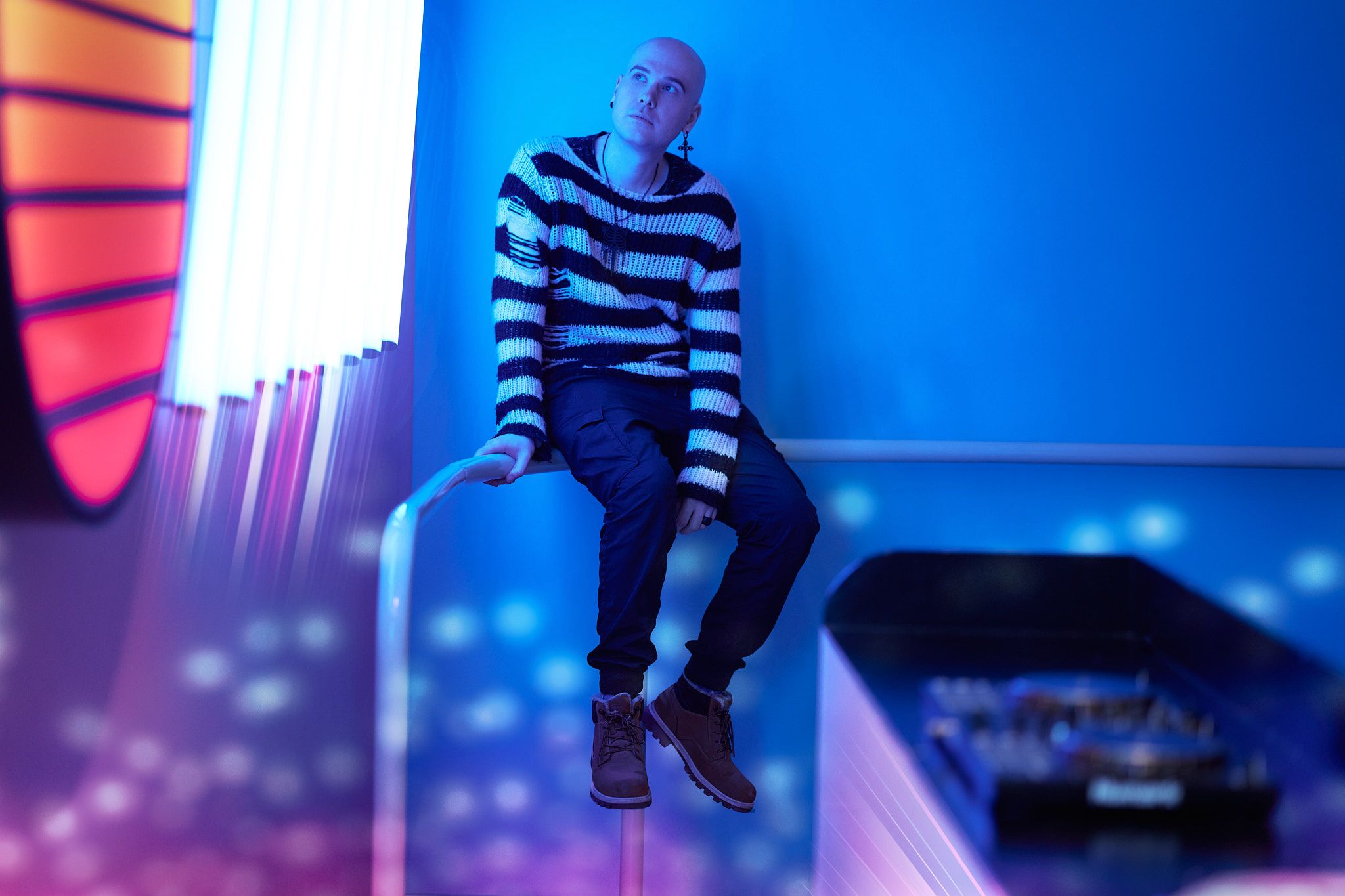 Person in striped shirt sitting on edge against blue-lit background.