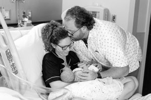 Black and white photo of new parents lovingly gazing at their newborn baby in hospital.