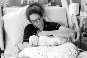 Black and white photo of new mother holding newborn baby in hospital bed after delivery.
