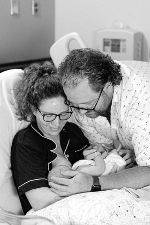 Black and white portrait of new parents bonding with their newborn baby in hospital room.