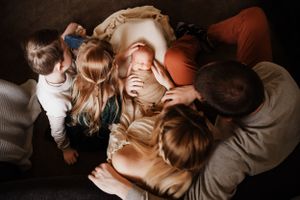 two parents holding baby on their lap surrounded by two young children putting hands on baby in Staten Island NY