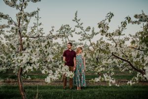 Couple poses together in flowering apple orchard during springtime photo session.
