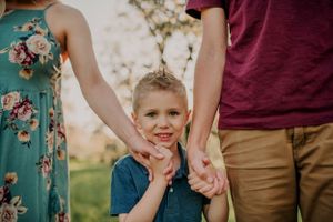 Child holds hands with adults while standing between them in an outdoor setting.