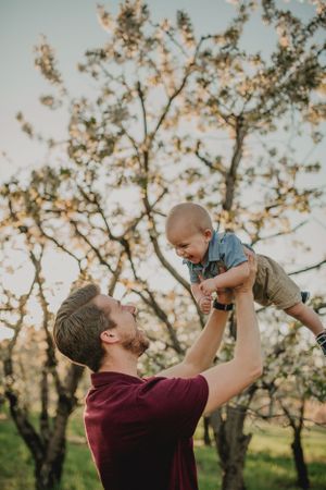 Adult lifts small child in the air against a backdrop of blooming spring trees.