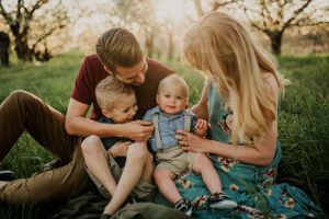 Candid family portrait on grass showing tender moments between parents and children in springtime.