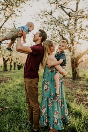 A loving family moment captured in a blooming orchard at sunset with playful interactions and a floral dress.