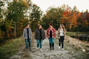 Group in plaid flannel shirts walking together on path through vibrant fall foliage.