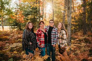 Family wearing coordinating plaid shirts poses together in autumn forest with golden sunlight.