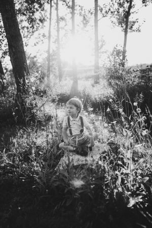 Child explores a sunlit meadow surrounded by tall trees in a dreamy black and white photograph.