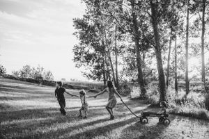 Family walking together along a tree-lined path pulling a wagon on a summer day.
