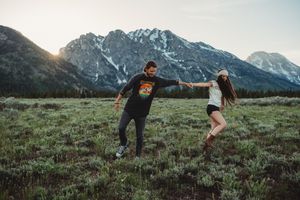 Couple playing and dancing in meadow with snow-capped mountains in background.
