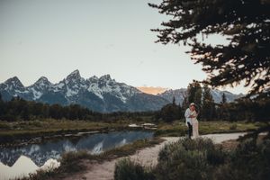 Romantic mountain landscape with couple standing by reflective lake at sunset.
