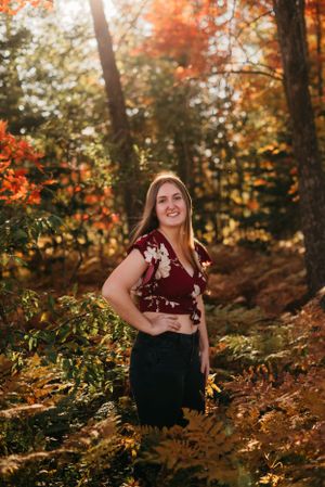 Portrait of woman in burgundy top surrounded by autumn foliage in sunlit forest.
