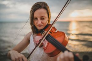Musician playing violin at sunset by the ocean.