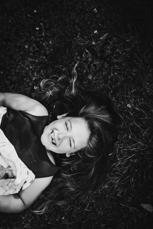 Person lying on grass laughing joyfully in black and white photography.