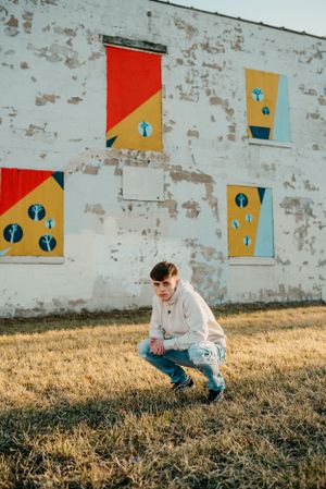 Person crouching in front of white wall with geometric art installations at sundown.
