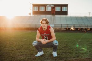 Athlete in red jersey crouches on football field during golden hour.