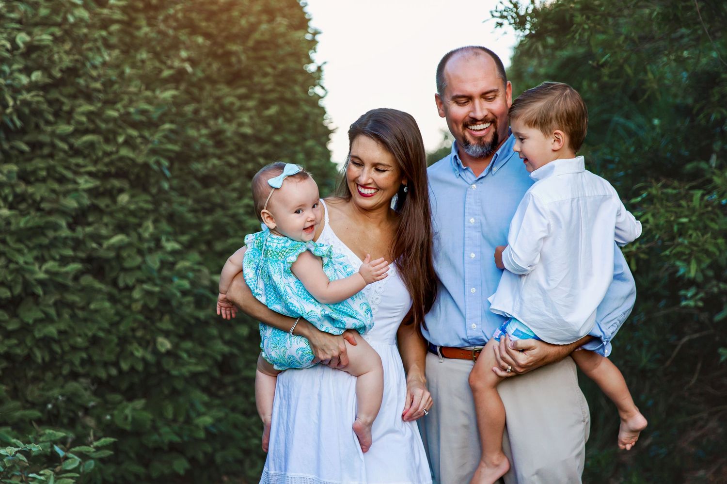Family portrait outdoors with greenery background in casual summer attire.