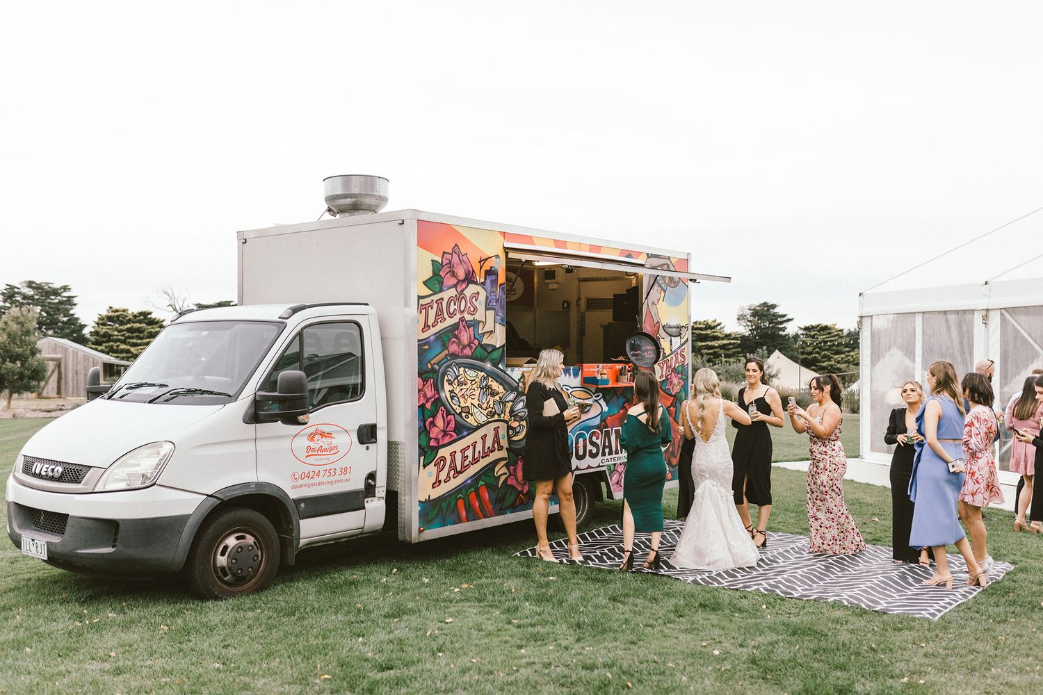 Colorful food truck serving guests at an outdoor wedding celebration on a grassy field.