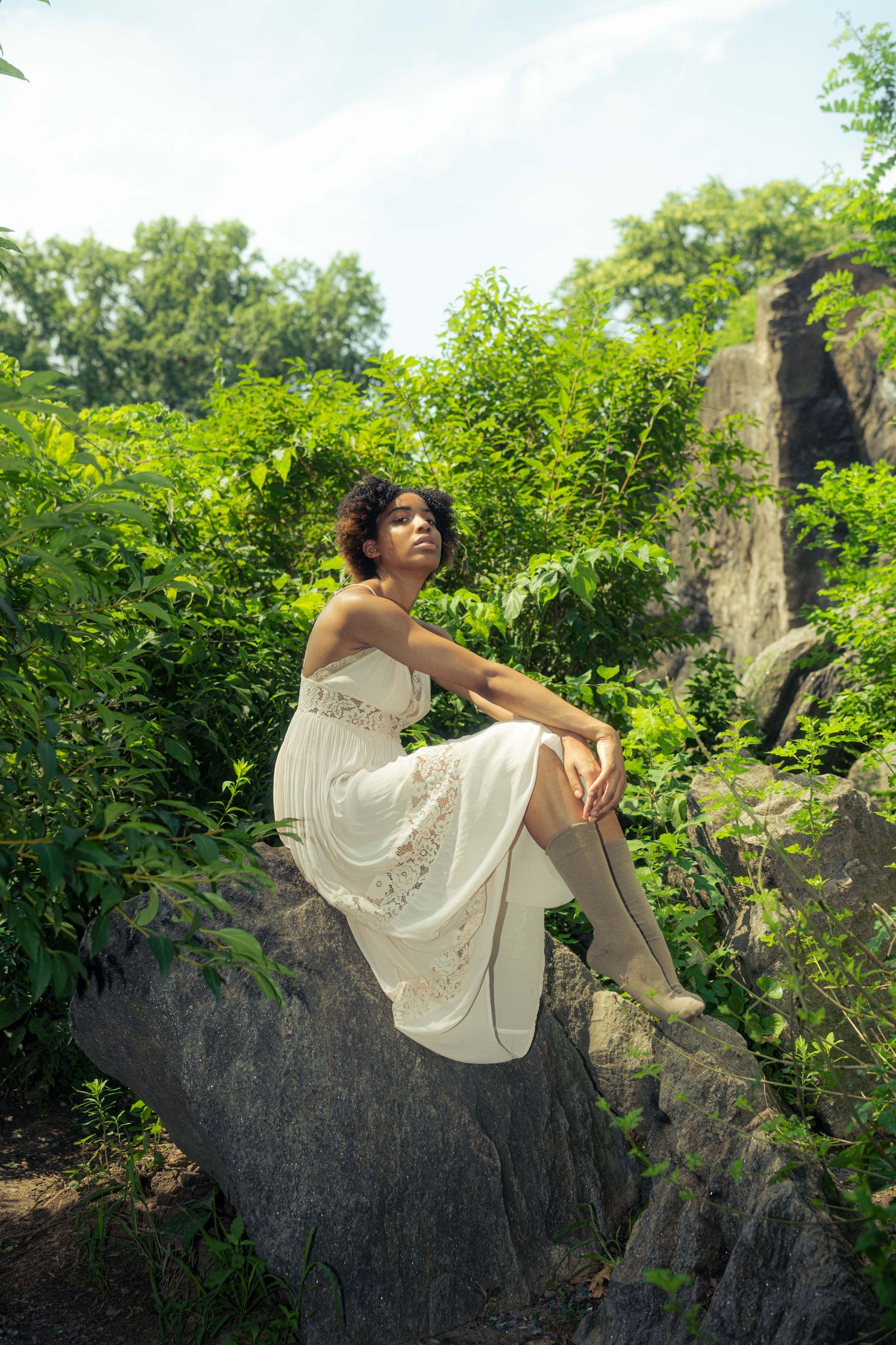 A white dress flows elegantly as someone poses on rocky terrain surrounded by lush greenery.