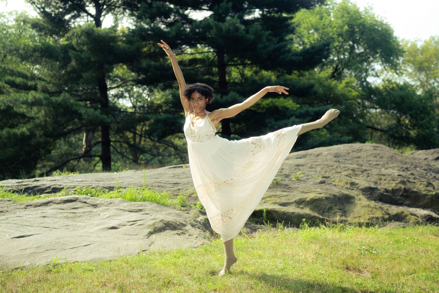 A dancer in white performs a graceful pose on a rocky outdoor stage.