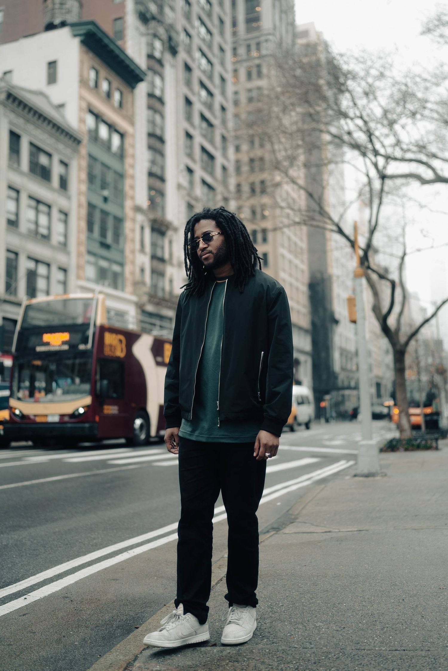 Wide angle street shots of someone wearing black clothing walking along a New York City avenue with tall buildings.