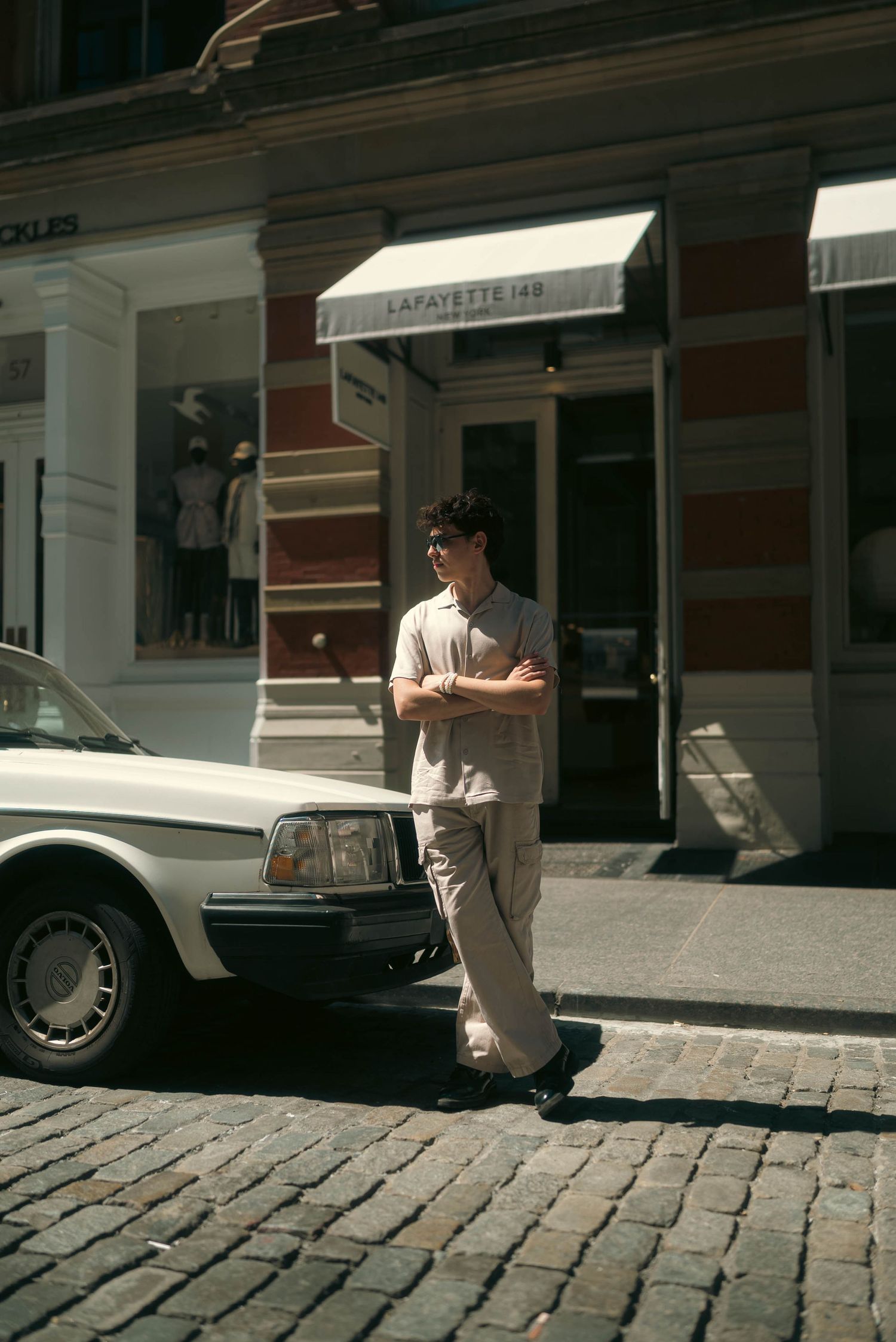 Casual street fashion portrait on cobblestone street with vintage car in background.