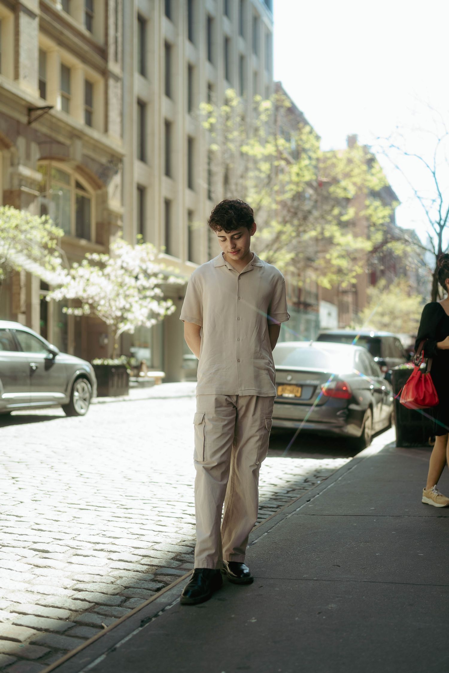 Urban fashion photograph on cobblestone street with modern buildings and parked cars.
