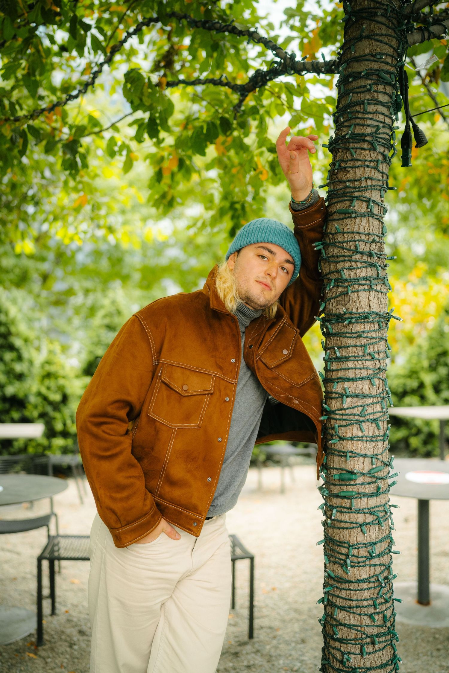 Casual autumn fashion portrait leaning against a tree wrapped in decorative lights.