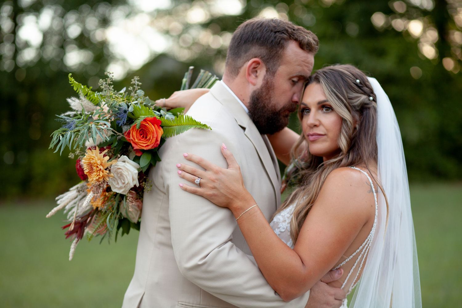 A loving couple shares an intimate moment during their outdoor wedding with a colorful autumn bouquet.