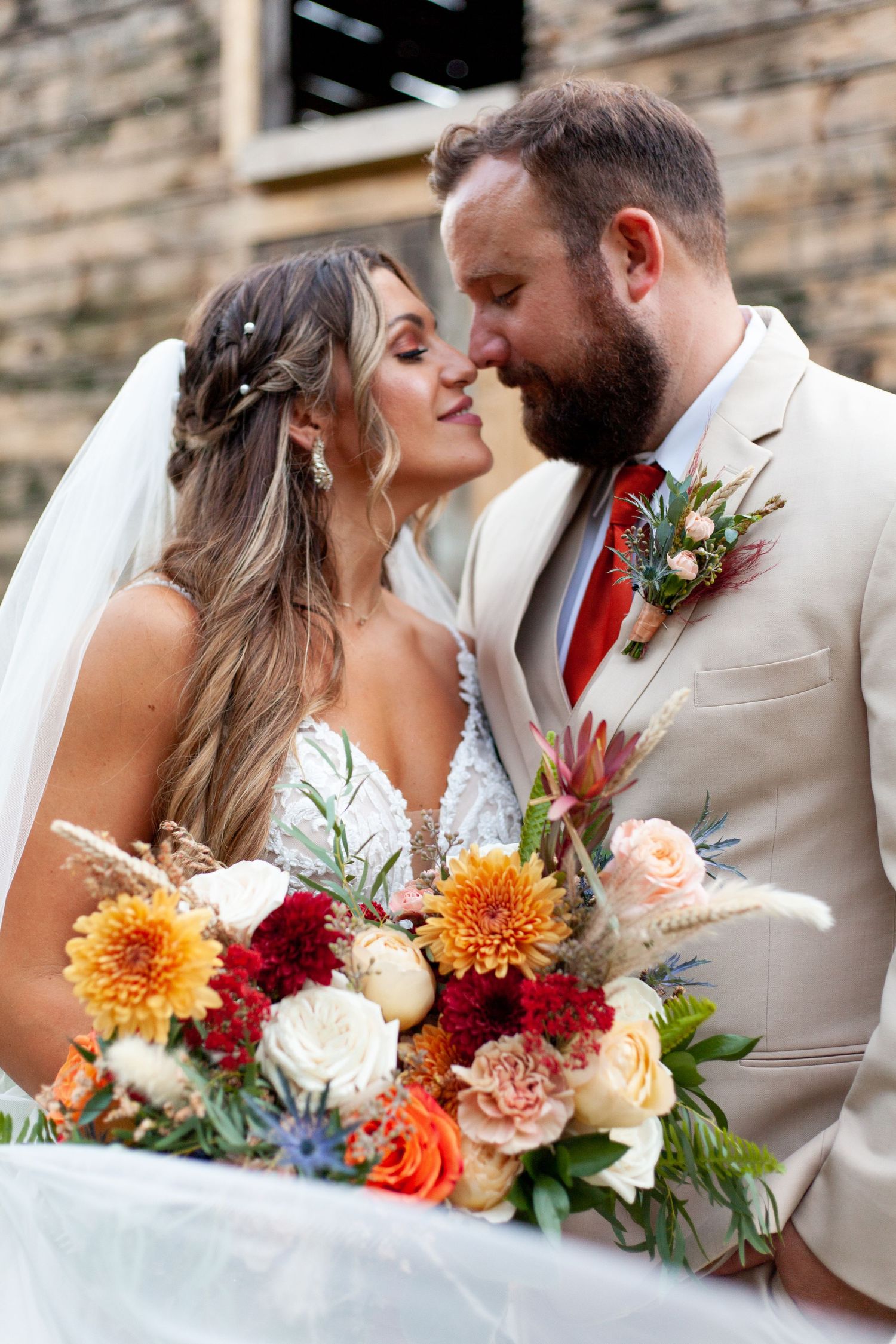Romantic autumn wedding couple sharing intimate moment with colorful fall bouquet featuring dahlias and roses.