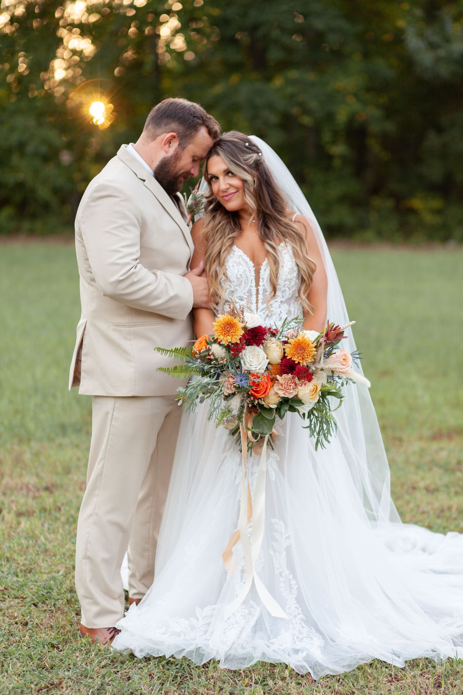 A couple shares an intimate moment at sunset in a garden setting with the bride holding a vibrant autumn bouquet.
