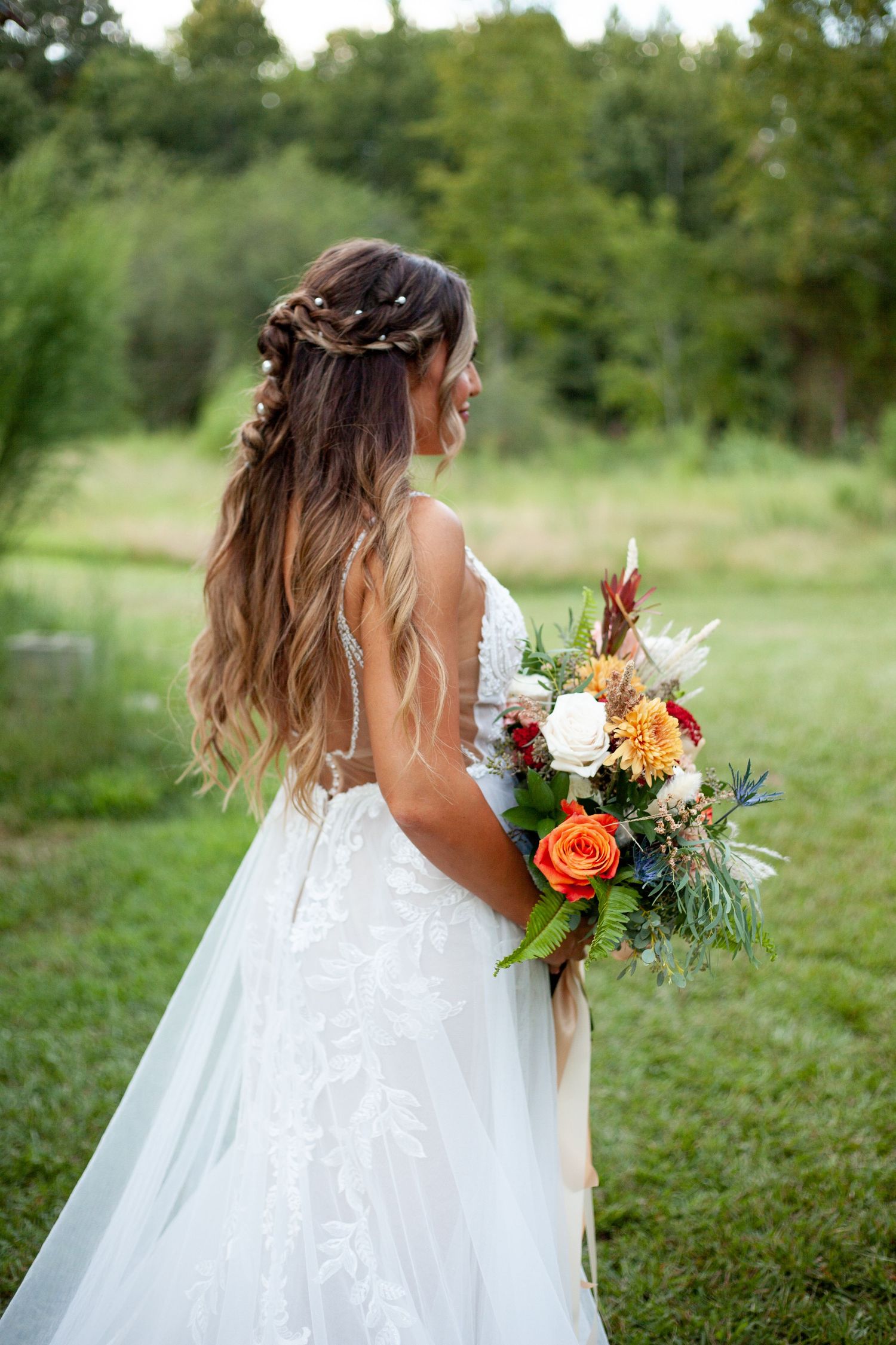 Bride with long wavy ombre hair and braided crown holds vibrant fall wedding bouquet in outdoor garden setting.