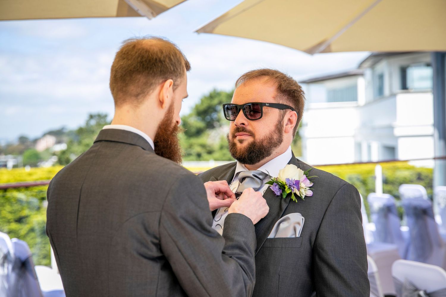 A boutonniere being adjusted outdoors on a sunny wedding day.