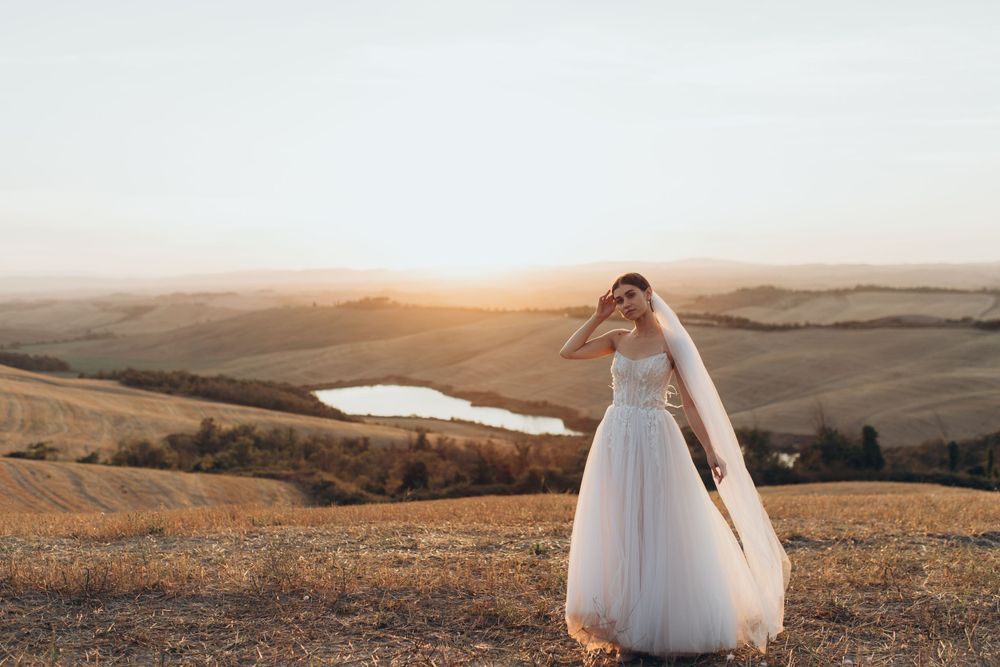 Romantic bridal pose with flowing dress and veil against rolling hills at golden hour.