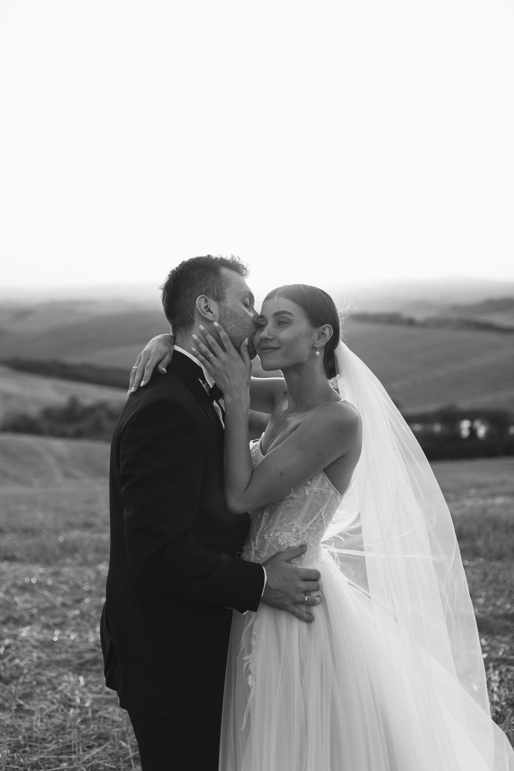 Intimate black and white portrait of newlyweds sharing a tender moment on a hillside.