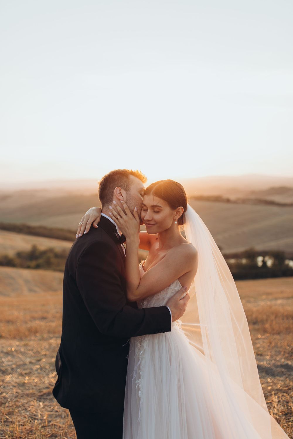 Golden hour wedding portrait captures an intimate embrace against a backdrop of rolling countryside.