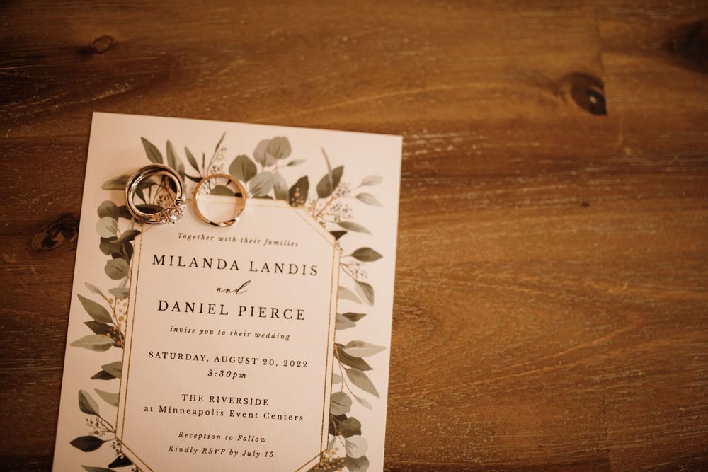 Wedding invitation for Milanda Landis and Daniel Pierce with gold rings on a wooden surface.