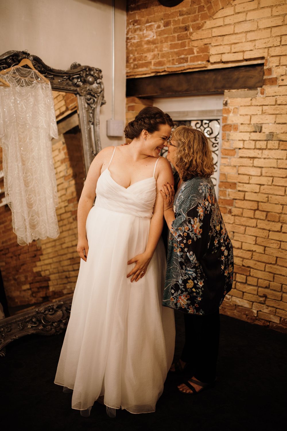 Tender moment between bride in white gown and mother sharing a forehead touch before the ceremony.