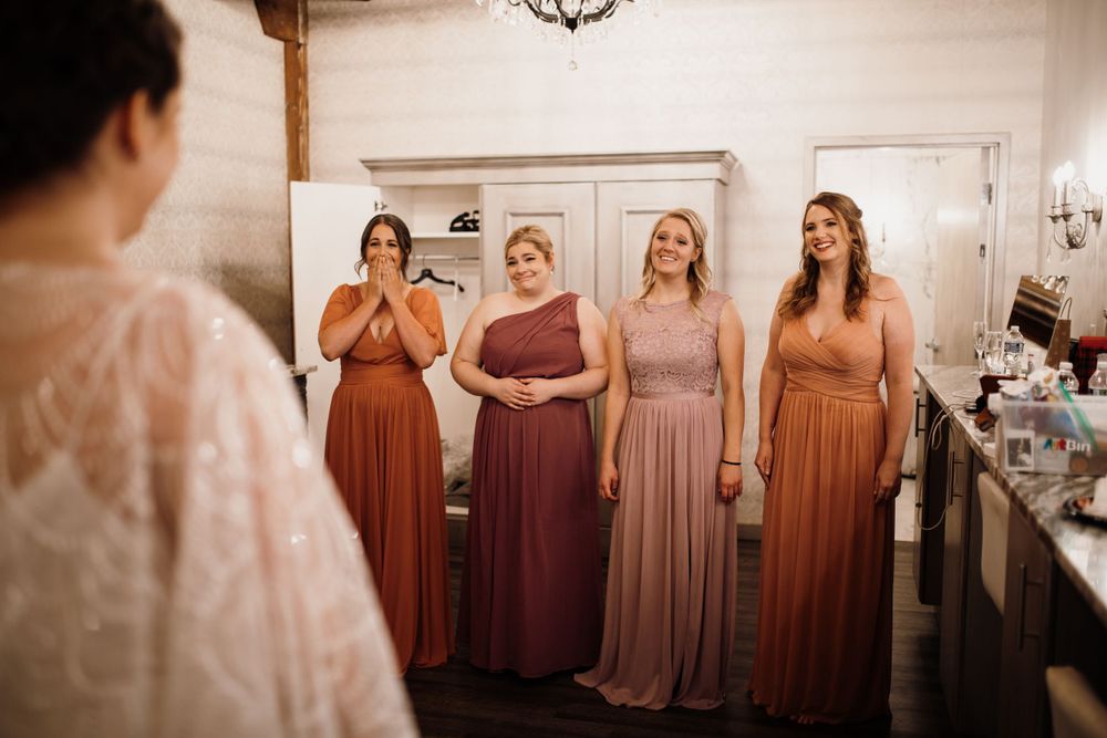 Bridesmaids in dusty rose and terracotta gowns react emotionally seeing the bride in her wedding dress.