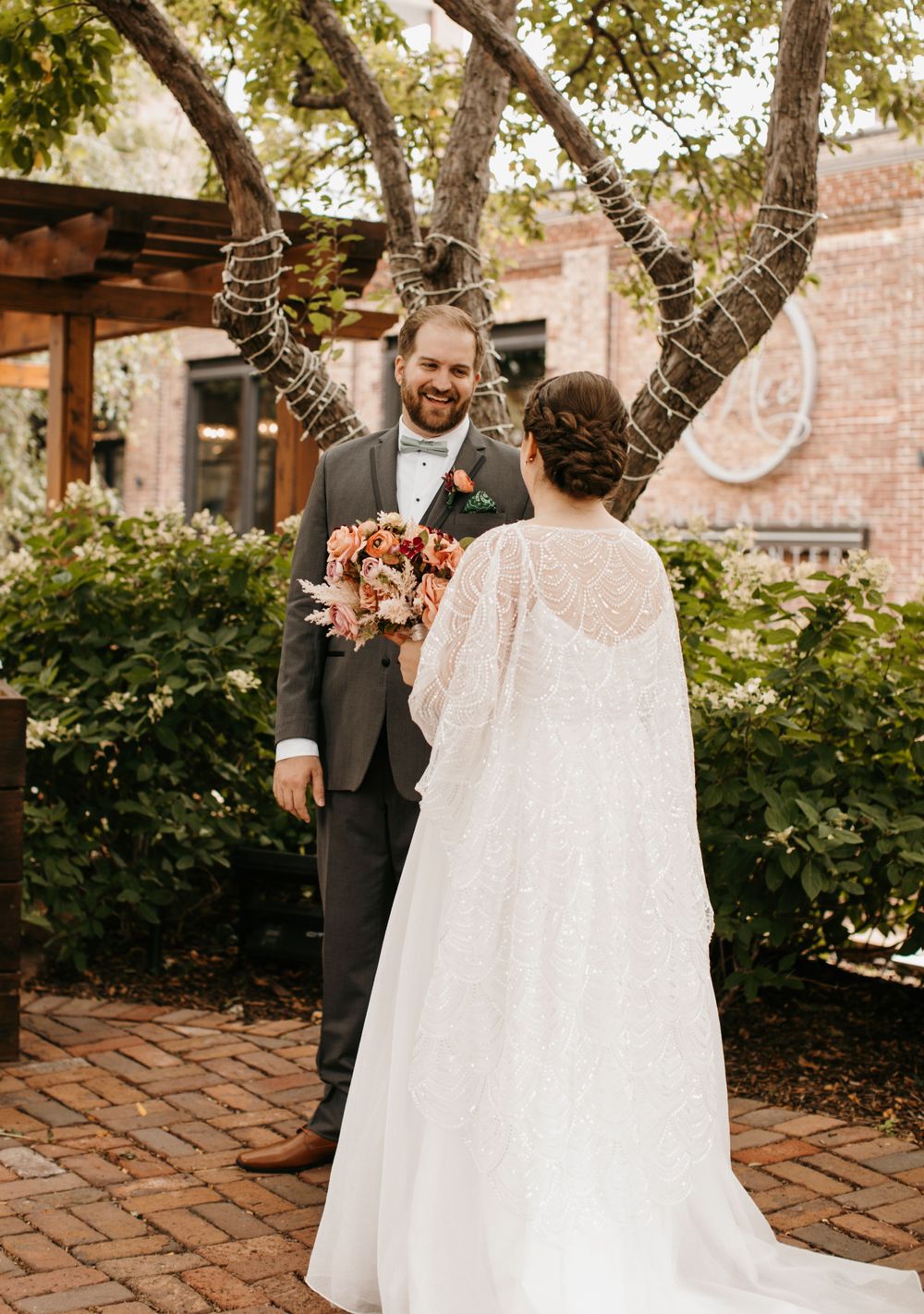Groom smiles joyfully at bride during outdoor first look surrounded by lush greenery.