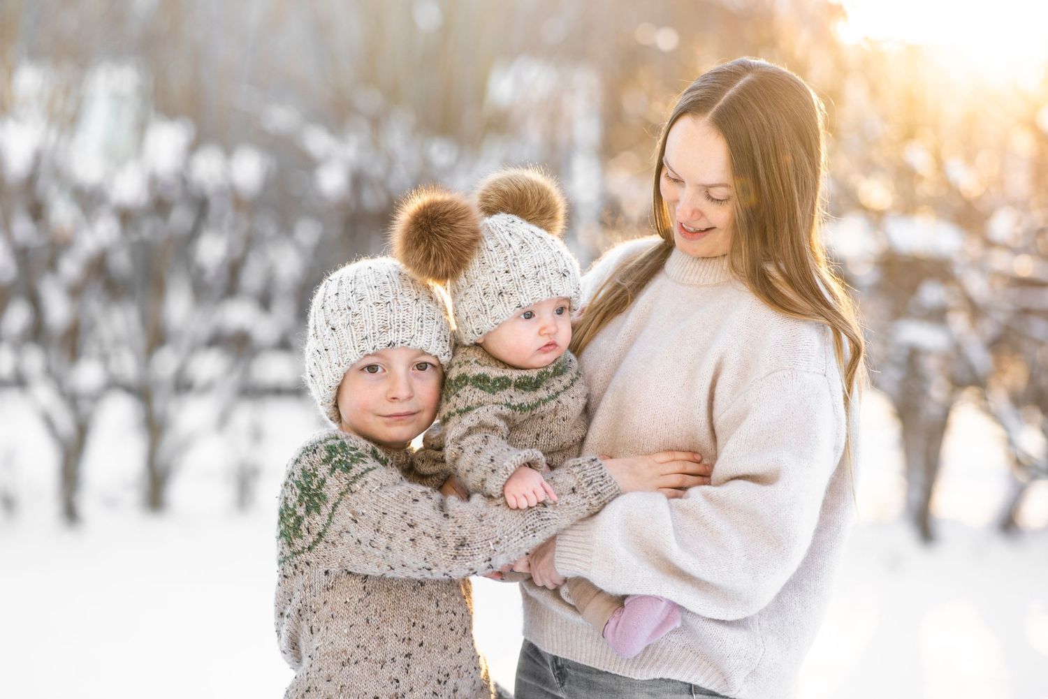 Family members embrace in snowy winter scene at sunset wearing cozy knit sweaters.