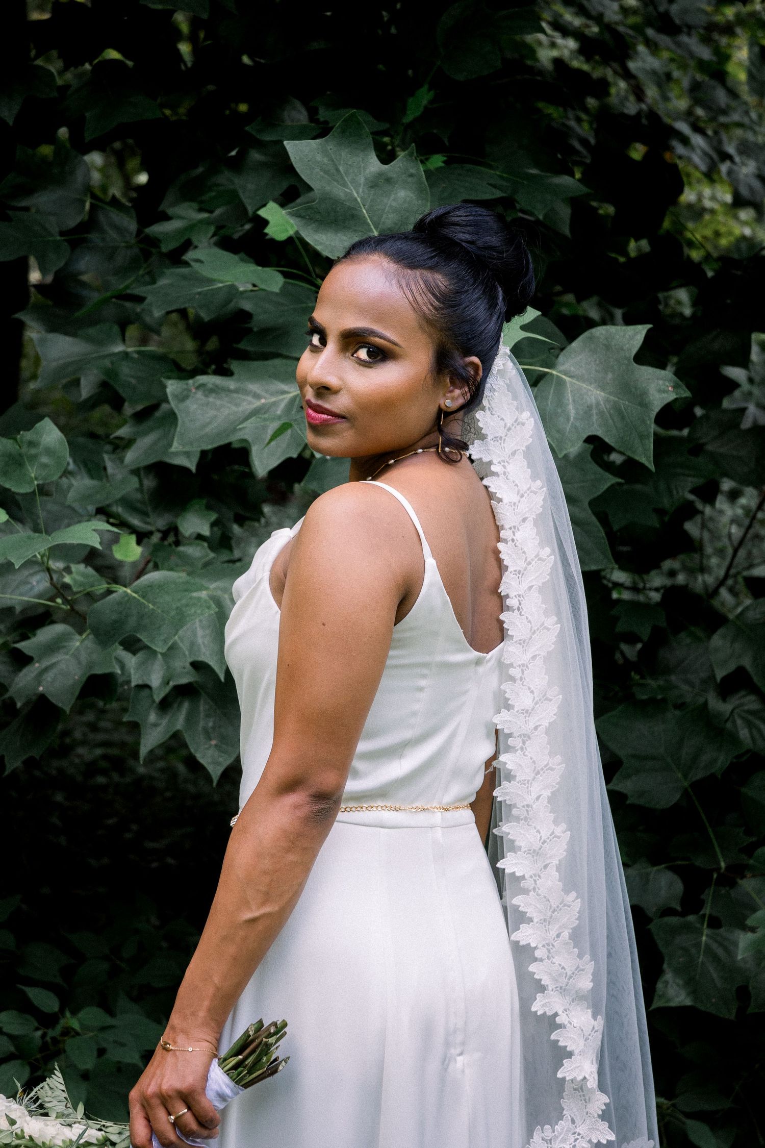 Bride in her wedding dress looking at the camera standing in front of greenery in Michigan