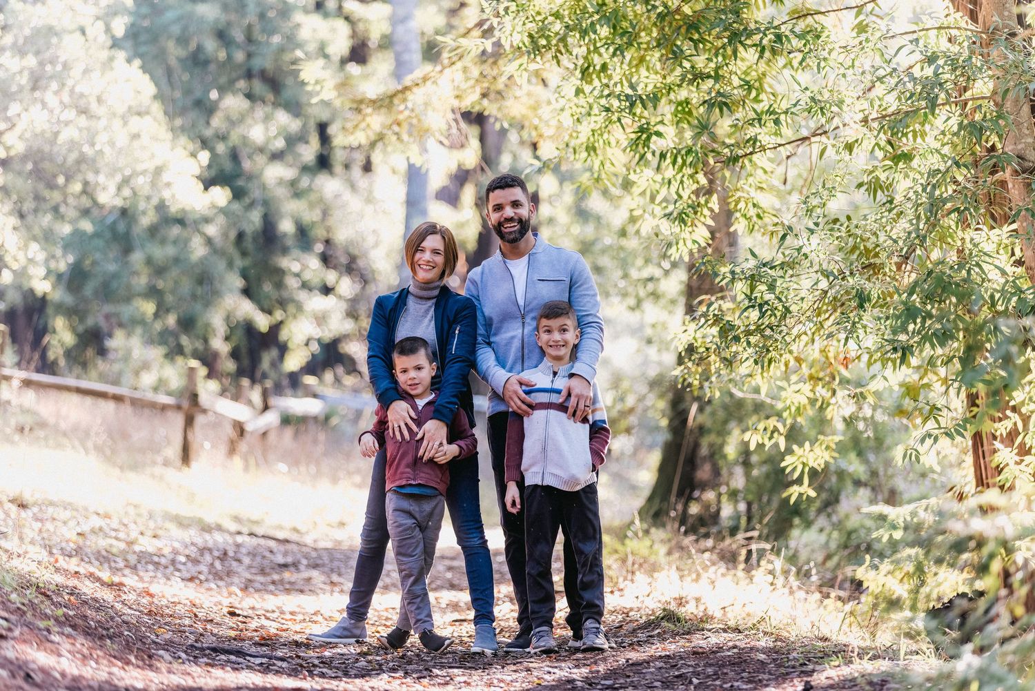Family standing together on a forest path surrounded by tall trees.